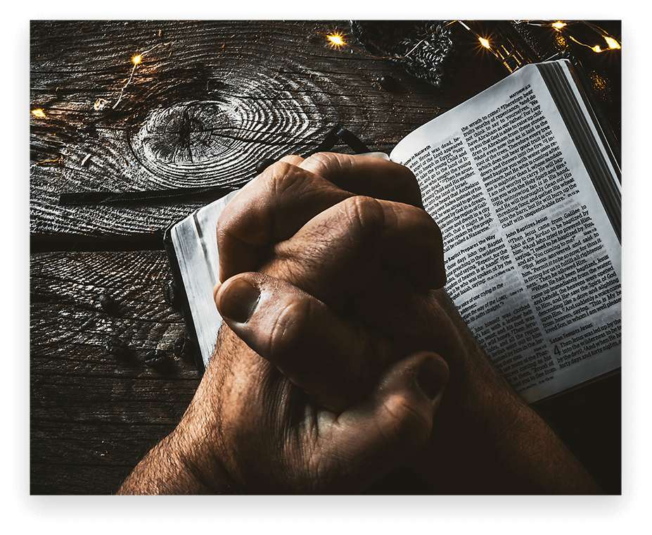 A person is praying with their hands on the bible.