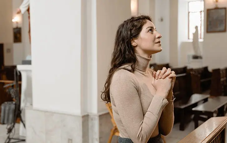 A woman standing in front of a wall with her hands clasped.